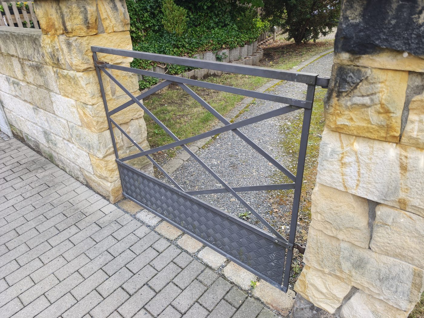 Metalltor mit Rautenmuster und Riffelblech zwischen zwei Sandsteinpfeilern